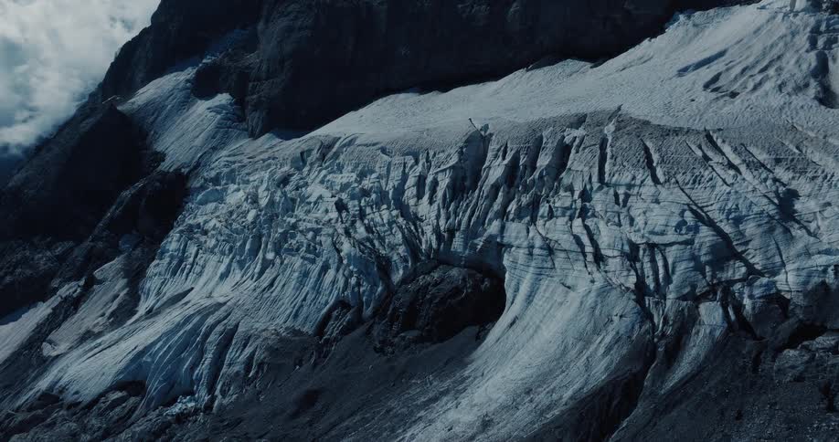 A dramatic, cold-toned shot reveals the textured surface of a mountain glacier
