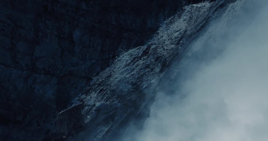 A moody vertical shot of water cascading down a dark, misty cliff face