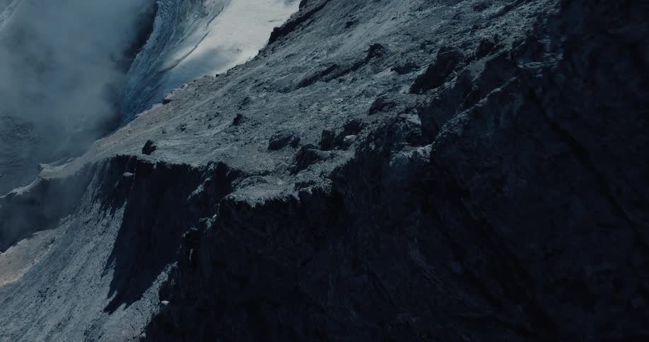 Dramatic aerial footage slowly moves along the dark, rocky, and smoking rim of a volcanic crater