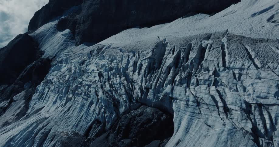 An aerial view slowly pulls back to reveal a lone climber navigating the vast, crevasse-filled surface of a mountain glacier