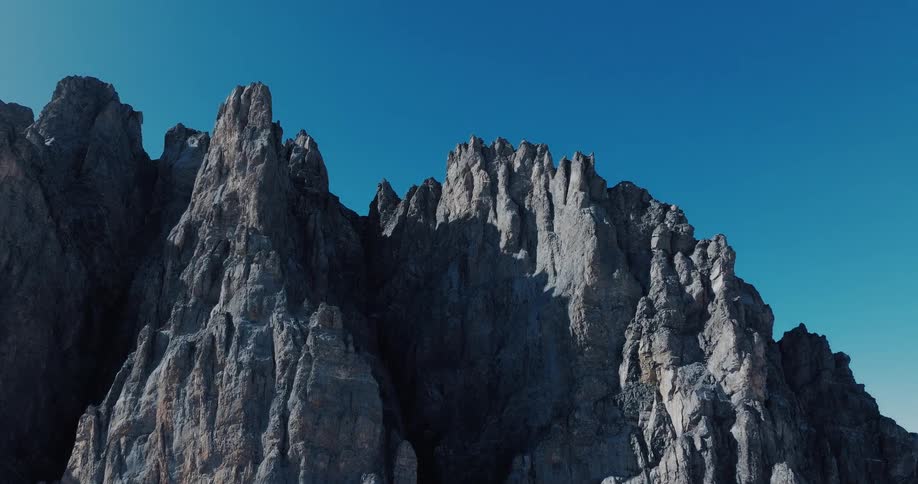 The rugged, rocky peaks of a mountain range stand tall against a clear, bright blue sky