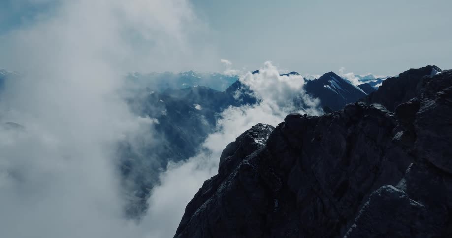 Slowly revealing a majestic, snow-capped mountain range from behind a rocky peak, with clouds drifting through the valley