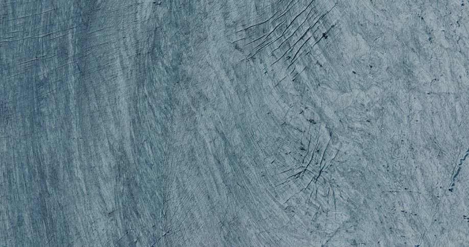 An aerial top-down slow zoom reveals the intricate cracks and patterns on the surface of a vast glacier
