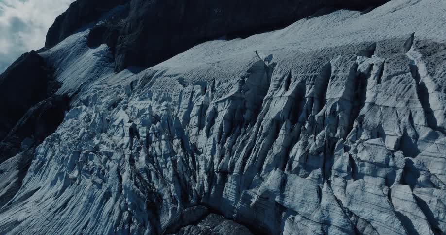A slow aerial zoom reveals the intricate crevasses and powerful textures of a vast mountain glacier