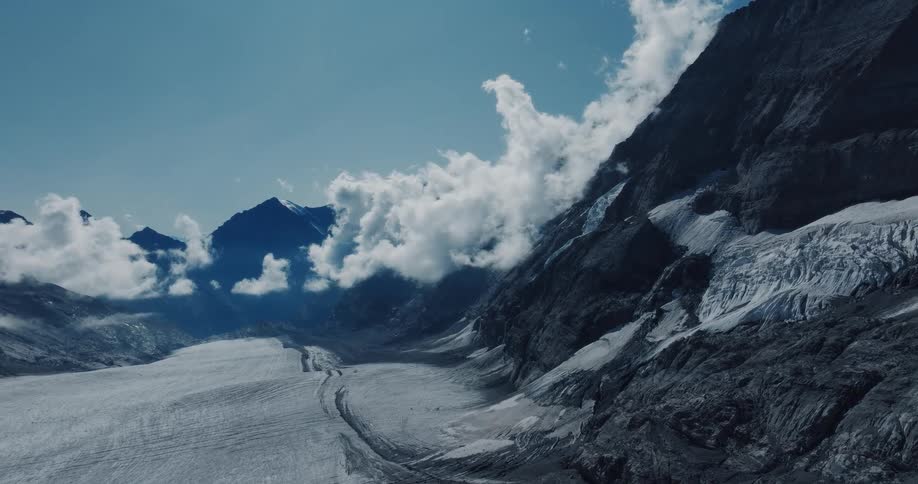 Majestic wide shot of a vast glacier carving a path through a rugged mountain valley as clouds drift by the peaks
