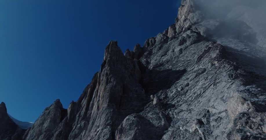 A determined rock climber carefully scales a sheer, jagged mountain face under a vast, clear blue sky