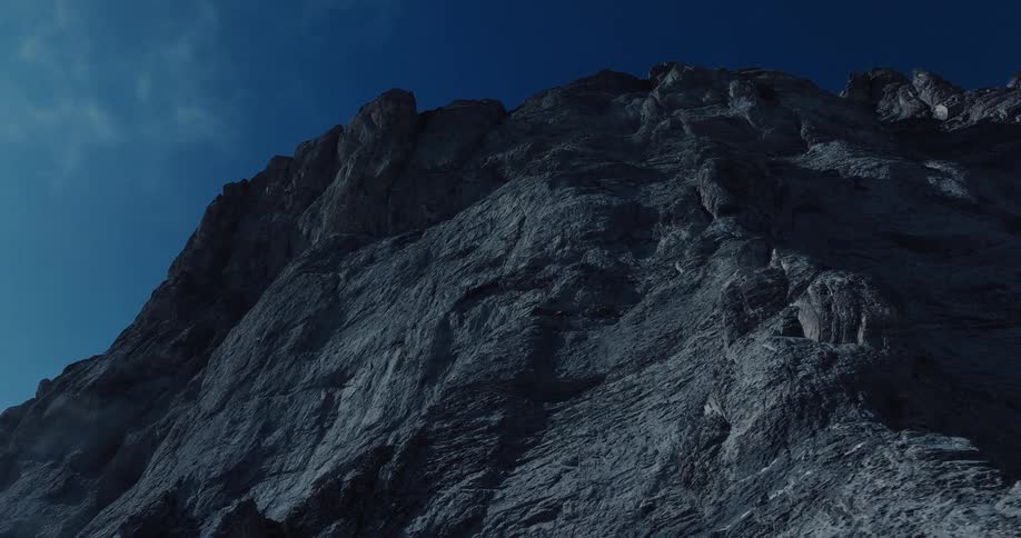 An imposing and shadowy mountain cliff face towers against the deep blue sky at night