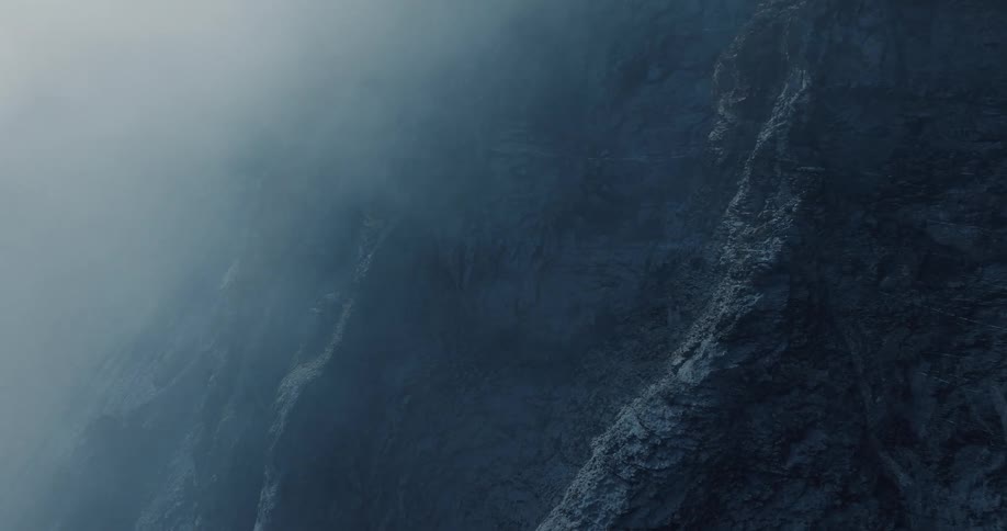 Thick fog moves over a dark and rugged rock face creating a mysterious atmosphere