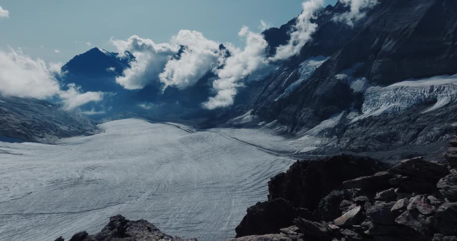 A breathtaking panoramic view reveals a massive glacier nestled between majestic, cloud-capped mountains