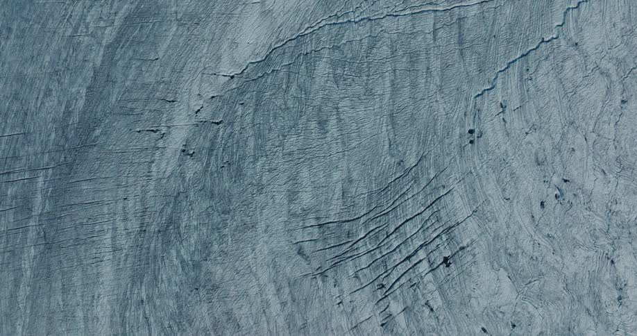 A mesmerizing top-down aerial view slowly ascends over a vast, textured glacier, revealing intricate patterns and deep crevasses in the ice