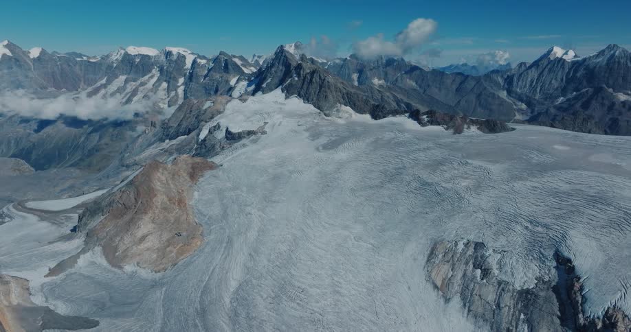 A majestic aerial panorama showcases a sprawling glacier and rugged, snow-covered mountains under a clear blue sky