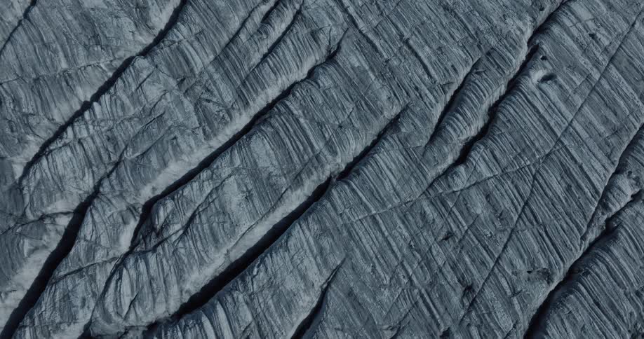 Close-up aerial footage captures the intricate, linear patterns and deep cracks on the surface of an ancient glacier