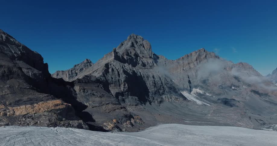 Stunning aerial footage pans across a vast glacier towards towering, rocky mountains on a sunny day