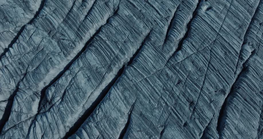 A static, top-down aerial view reveals the abstract textures and patterns of a striated rock formation