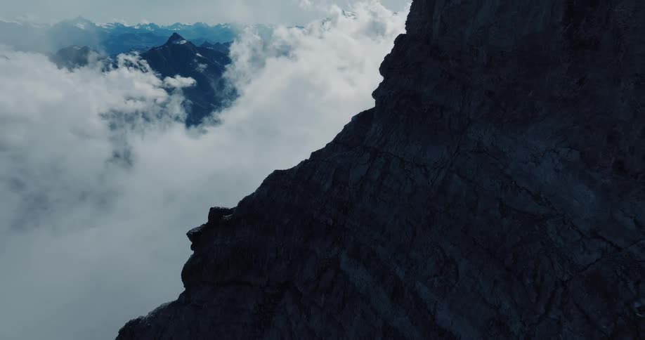 A breathtaking high-altitude view from a shadowed mountain cliff over a sea of clouds and distant alpine peaks
