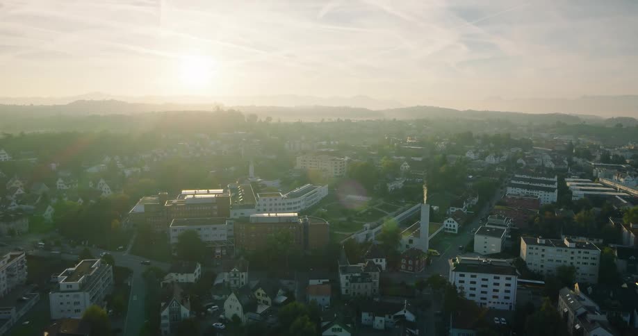 A slow aerial pullback reveals a sprawling European town bathed in the hazy golden light of an early morning sunrise