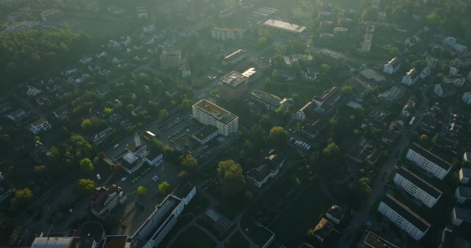 A static high-angle aerial view of a quiet suburban town waking up at sunrise with a golden haze