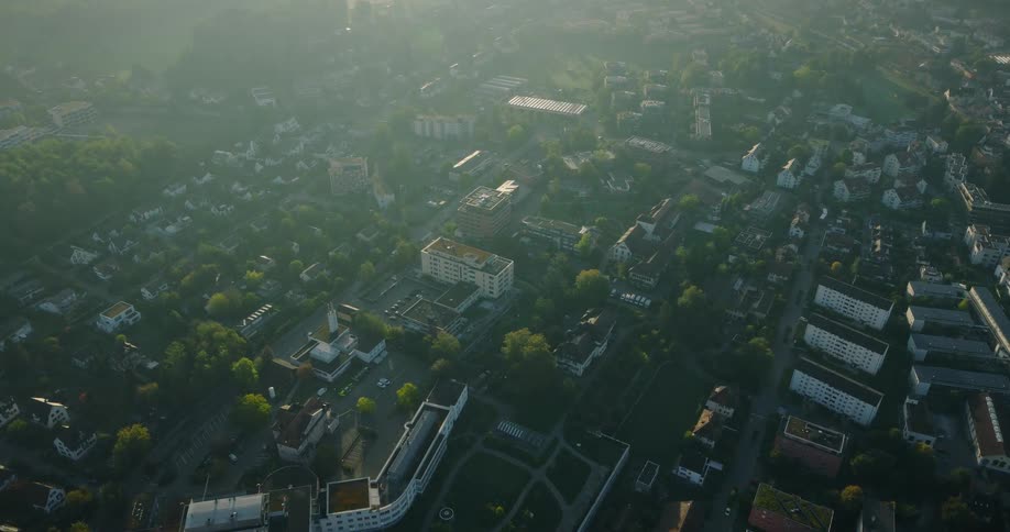 A high-angle aerial view shows a serene town bathed in the beautiful, hazy golden light of a calm morning sunrise