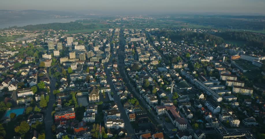 An expansive aerial view of a Swiss city with a lake in the background during the early morning hours