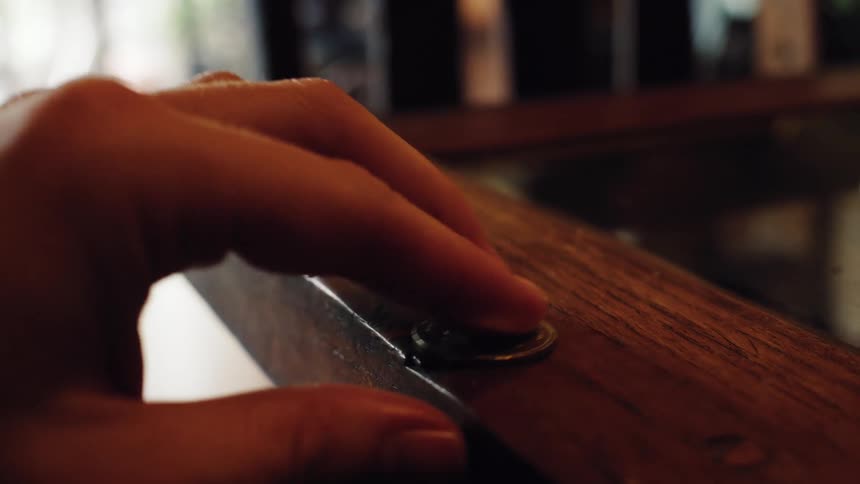 A slow-motion close-up shot of a hand picking up a Japanese 100 Yen coin from a wooden surface