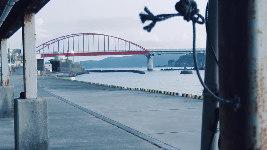 A quiet, overcast day at a pier with a red arched bridge spanning the water in the distance