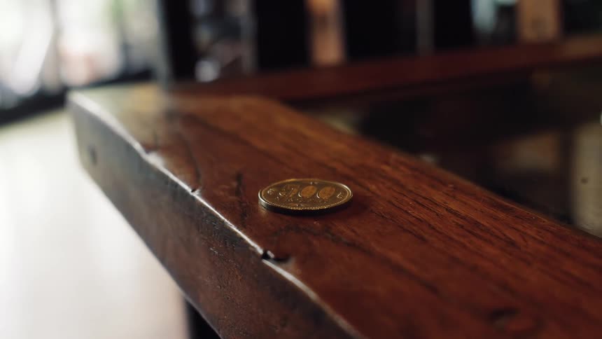 A hand in slow motion gently places a 500 yen coin on the corner of a rustic wooden table