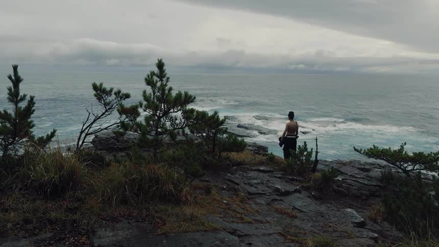 A traditional Japanese warrior contemplates the crashing waves from a clifftop on a moody, cloudy day