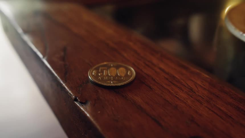 A still life close-up of a single 500 Japanese Yen coin on a polished dark wood table