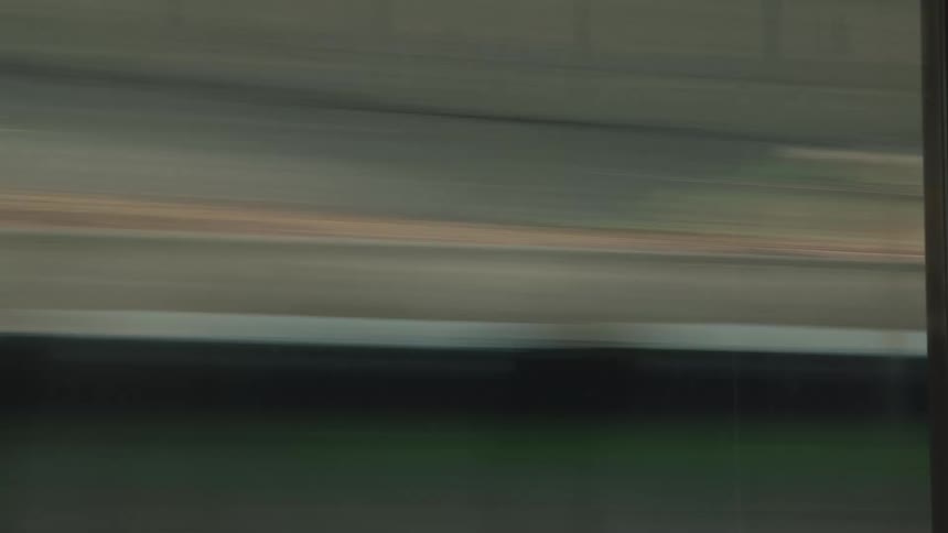 A motion-blurred point-of-view shot from a fast-moving train as it speeds past a green landscape and enters a dark tunnel