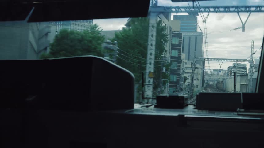 The view from a moving train reveals the cityscape of a Japanese city on an overcast day