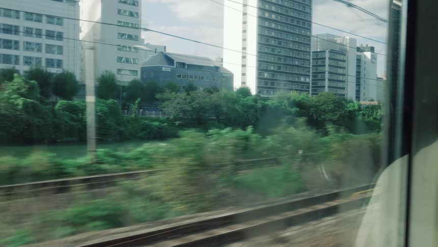A passenger's view from a train window as it emerges from a dark tunnel into the daylight, revealing a cityscape with a river