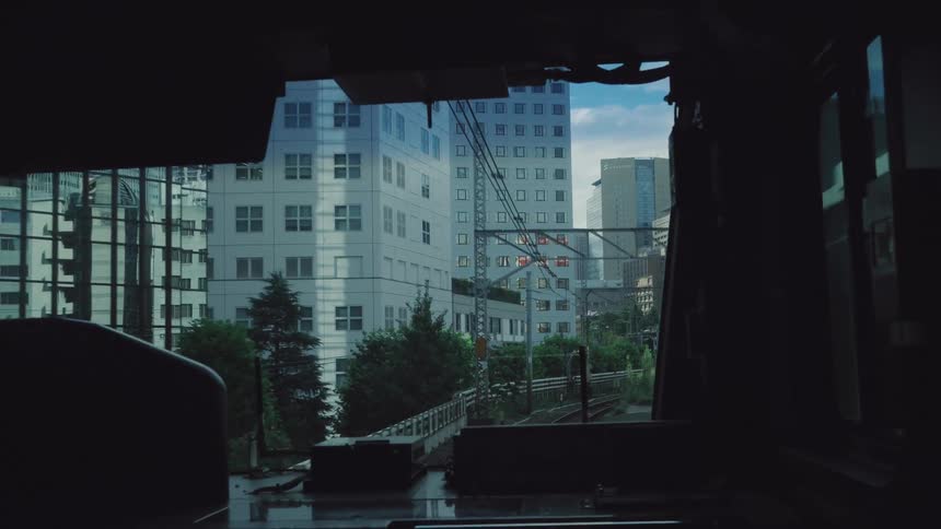 A cinematic view from the front of a moving train as it travels along elevated tracks through the city of Tokyo