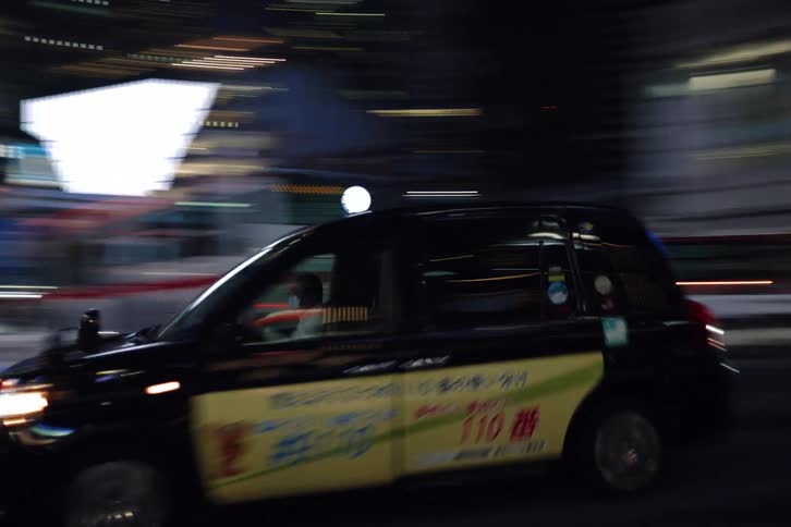 Tracking shot follows a black taxi cab as it drives through the city streets of Japan at night