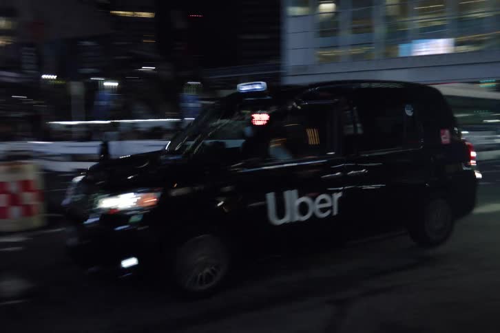 A sleek black Uber taxi cruises through the vibrant, illuminated streets of a modern city at night