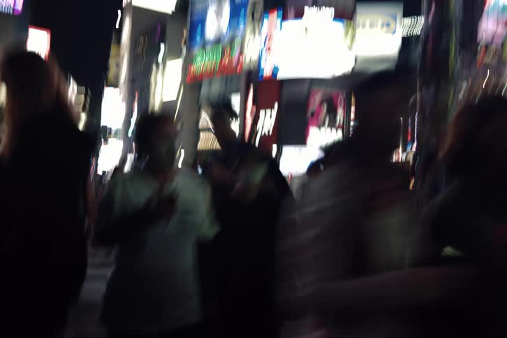A dizzying and blurry first-person view of walking through a crowded street in a brightly lit Asian metropolis at night
