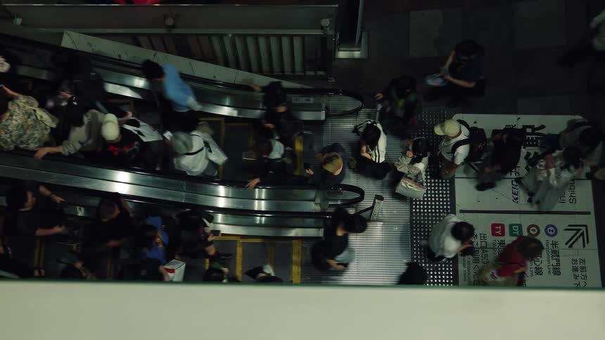 A top-down view of a bustling crowd of commuters riding an escalator in a busy public transit station