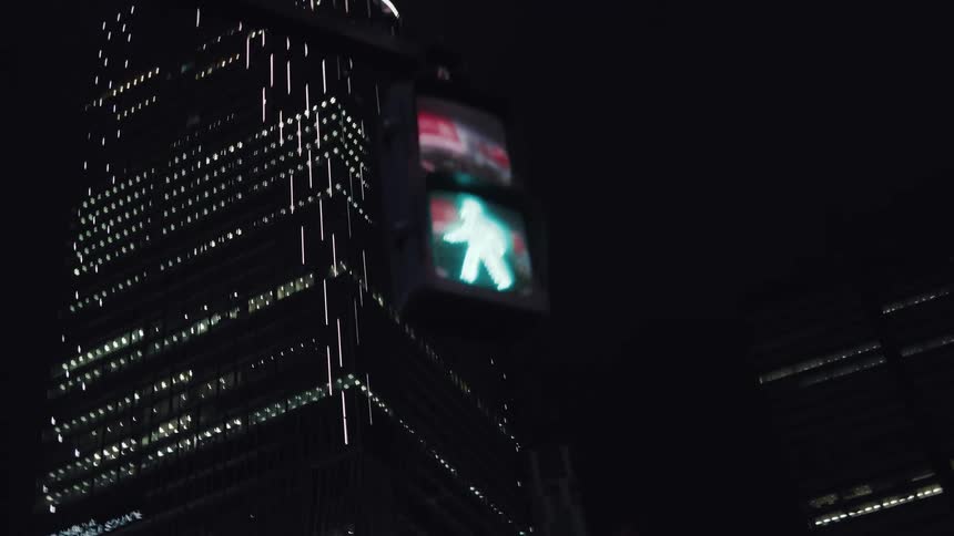 A pedestrian traffic light cycles from green to red at night with a brightly lit modern skyscraper in the background