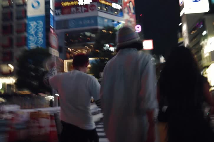 Blurry, shaky handheld footage follows a group of friends walking through the neon-lit streets of Shibuya, Tokyo at night