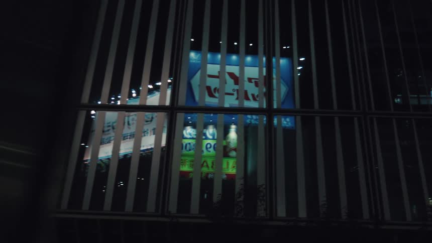 A cinematic reveal of glowing city billboards at night as seen through a slatted window
