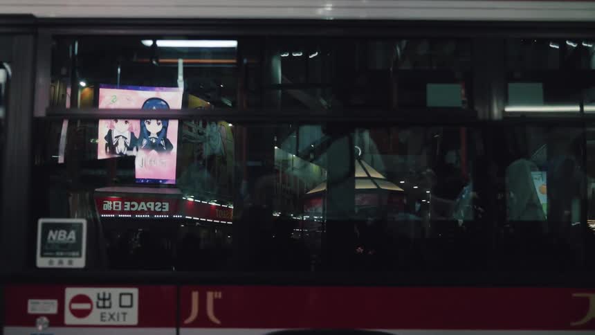 Colorful neon city lights with anime advertisements reflecting in the side of a city bus at night