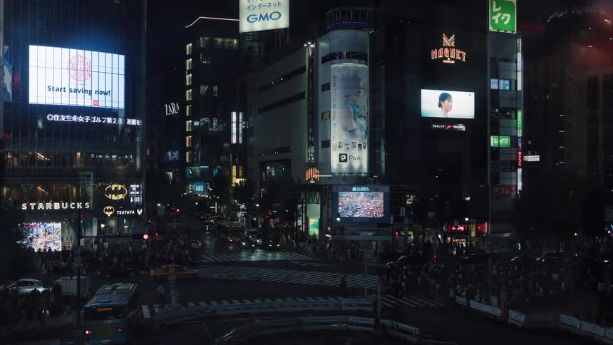 A static shot of the iconic Shibuya Crossing in Tokyo at night, with crowds and traffic moving through the intersection under glowing billboards