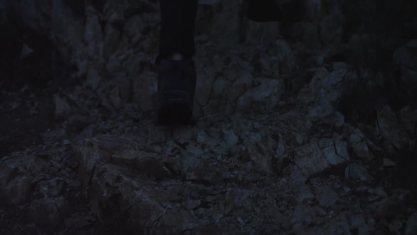 Slow-motion close-up of a hiker's boots treading carefully on a rocky mountain path at dusk