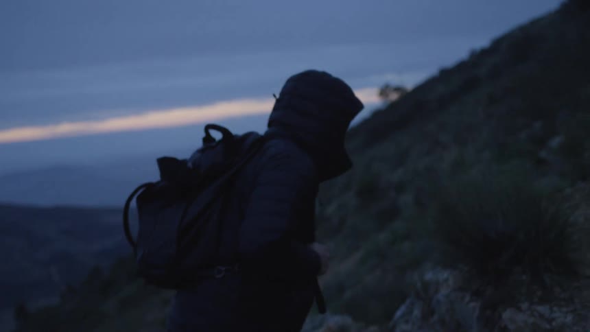 Slow motion shot of a hiker with a backpack ascending a mountain trail during the blue hour at dawn