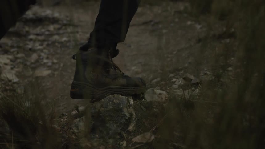 A close-up slow-motion shot of hiking boots walking along a rocky and dusty trail