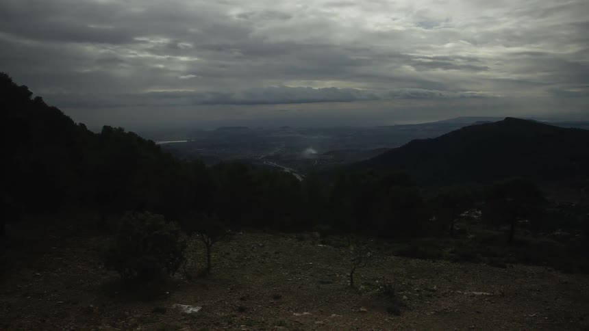 A gloomy view of a sprawling valley and distant mountains under an ominous, overcast sky