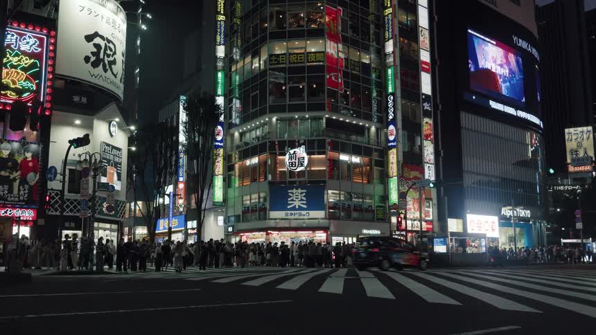 Vibrant neon signs illuminate a bustling Tokyo intersection as cars and taxis drive by at night