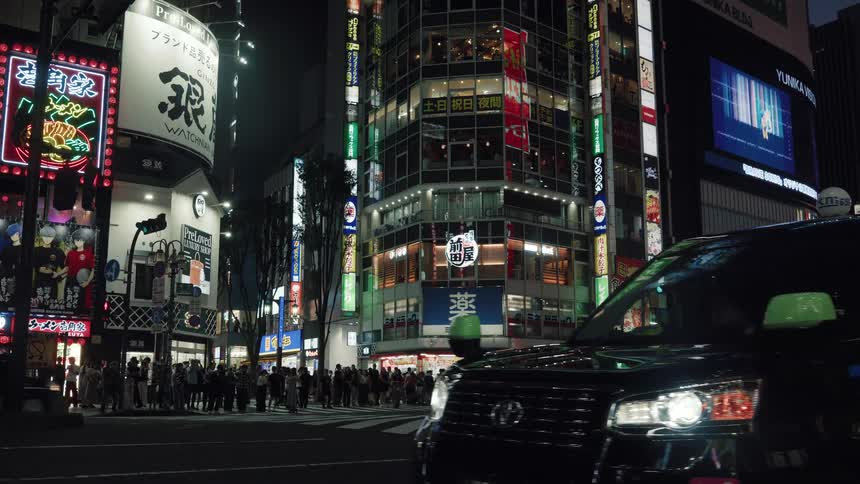 A black taxi cab pulls up to a busy intersection in Ginza, Tokyo at night, with bright neon signs illuminating the cityscape