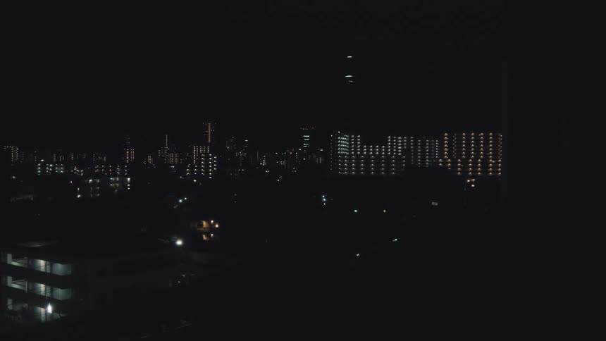A quiet city skyline with illuminated apartment buildings against the pitch-black night sky