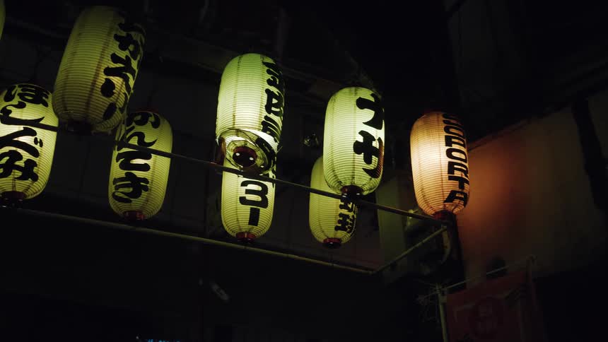 Illuminated Japanese paper lanterns with calligraphy hang in a dark urban setting at night