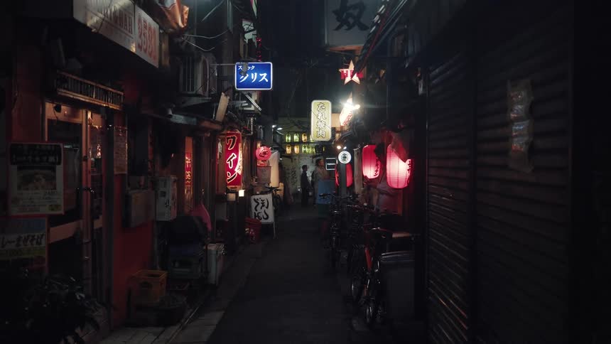 An atmospheric static shot of a narrow Japanese city alley at night, illuminated by glowing red lanterns and various signs